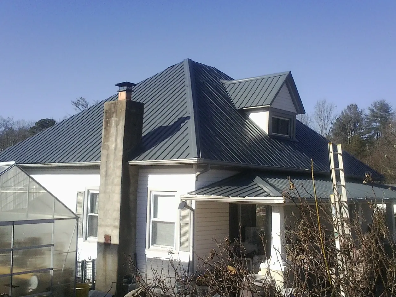 Dark blue standing seam metal roof on a white farmhouse with dormer — Slate & Tile Roof Repair by Roofing Brothers in Clendenin