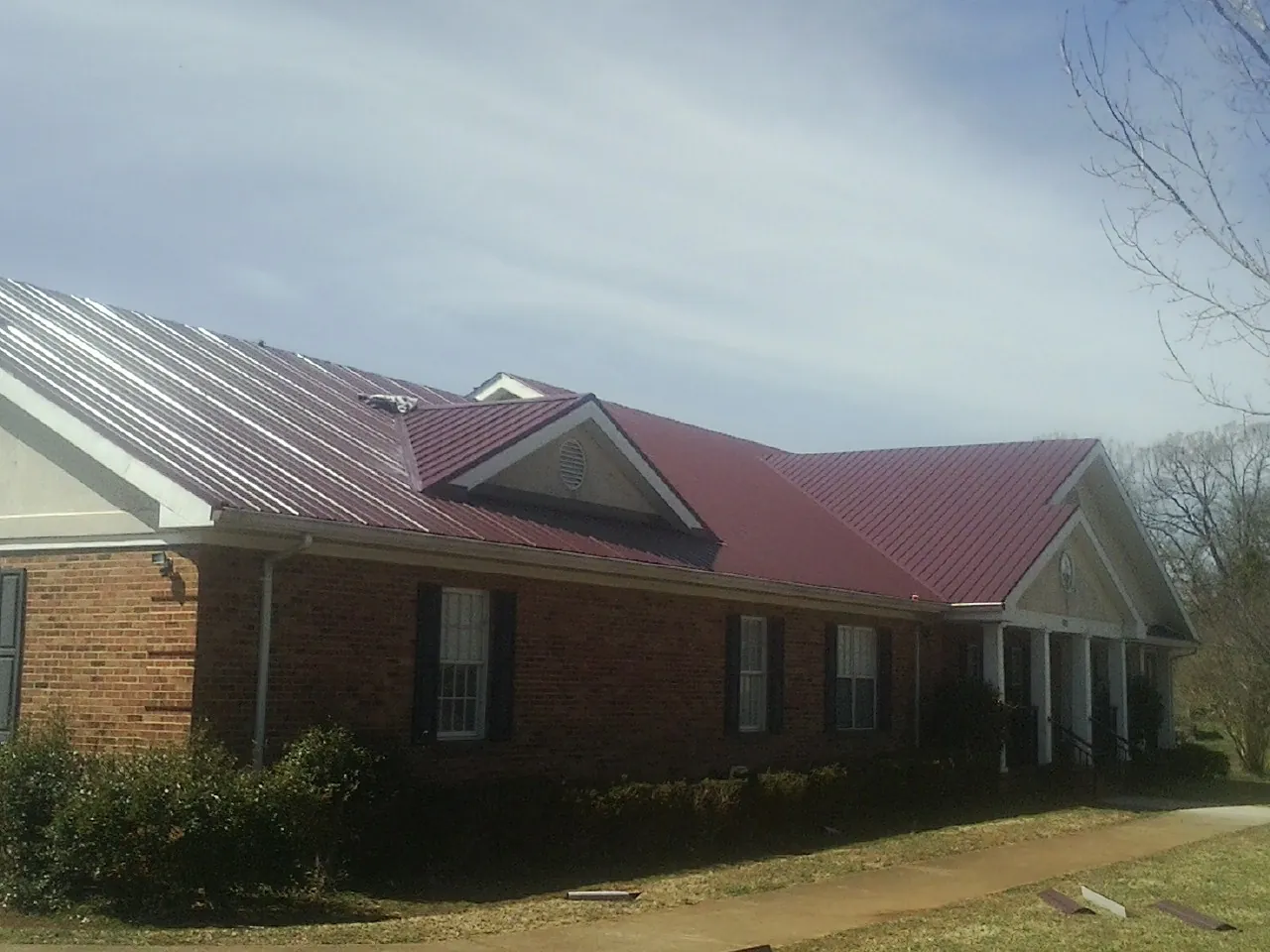Red metal roof with gabled entries on a long brick building, from a Hail Damage Roof Repair job in Clendenin