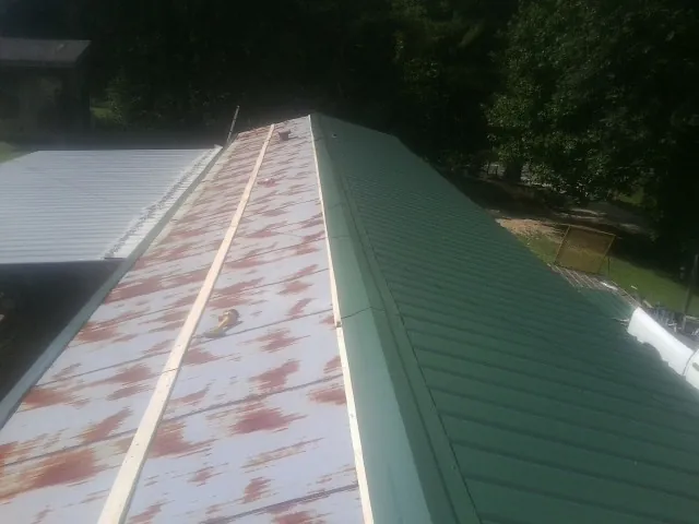 Old rusted panels beside newly installed green metal roofing — Wind Damage Roof Repair by Roofing Brothers in Clendenin