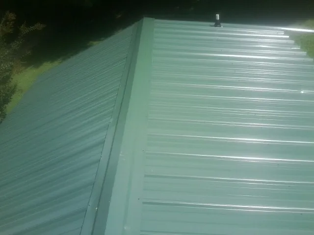 New green metal panels meeting at the ridge of a roof — Flat Roof Repair work by our crew in Clendenin