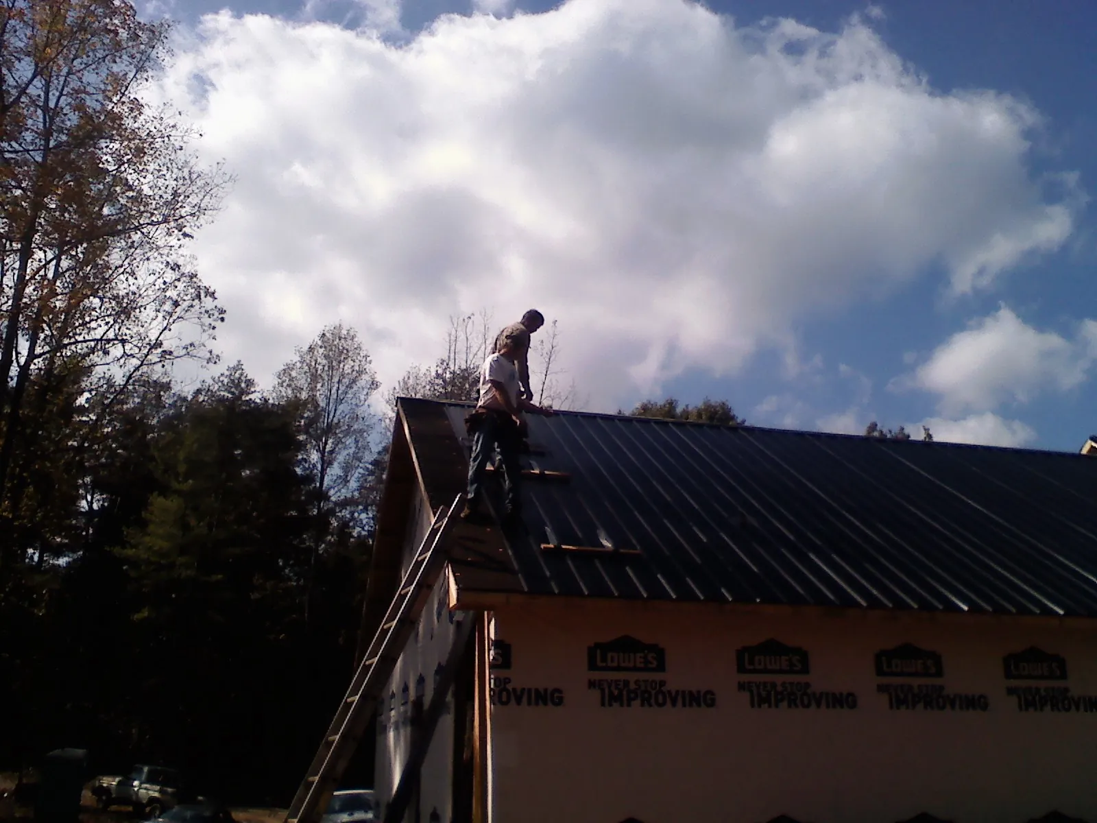 Roofer fastening dark metal panels high against a cloudy sky, from a Roof Inspection job in Clendenin