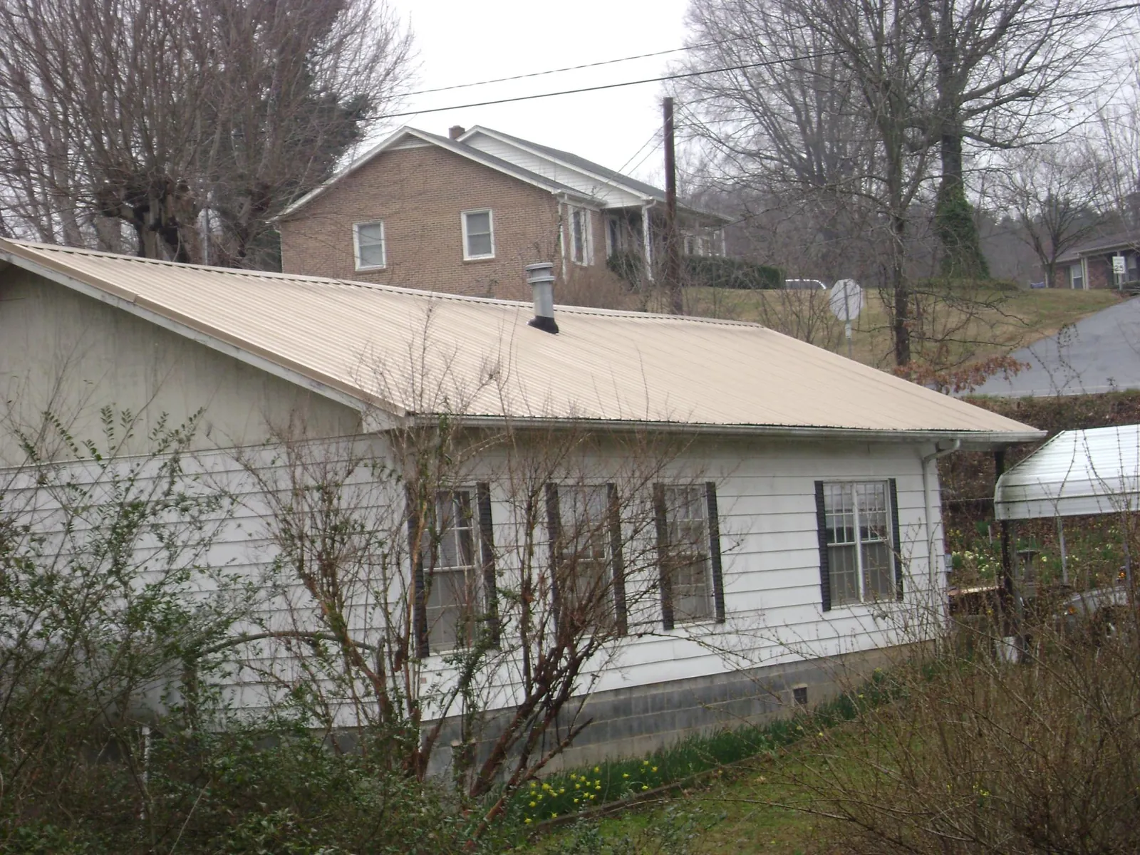 Tan metal roof on a white sided house set into a hillside — Commercial Roofing by Roofing Brothers in Clendenin