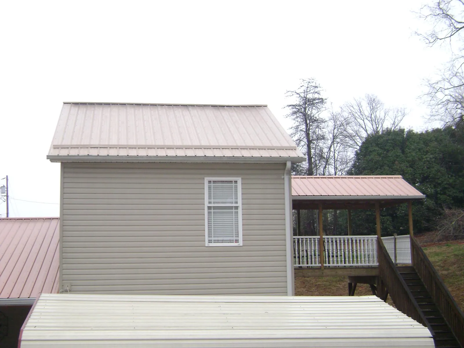 Tan metal roofs on a two story addition and attached porch, from a Roof Replacement job in Clendenin
